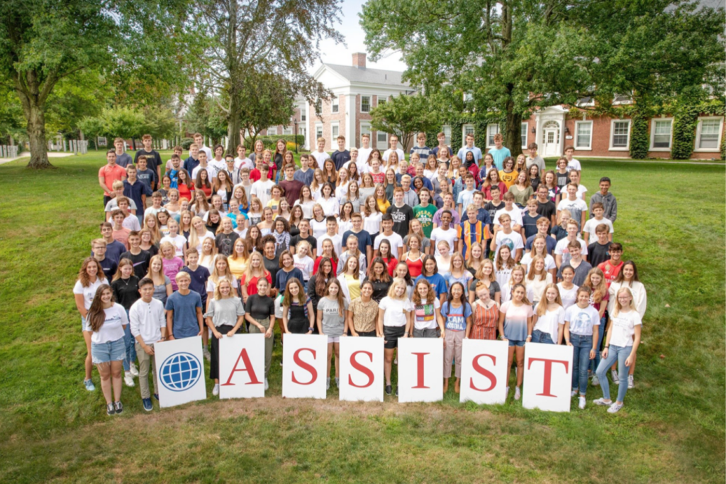 Class of ASSIST Scholars standing on a hill at a boarding private school in the United States holding signs that spell out ASSIST