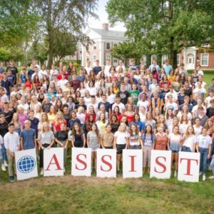 Class of ASSIST Scholars standing on a hill at a boarding private school in the United States holding signs that spell out ASSIST