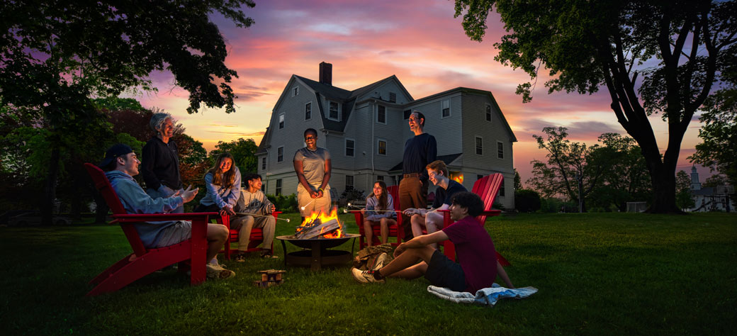 A group of students gathered around a campfire during sunset roasting marshmallows
